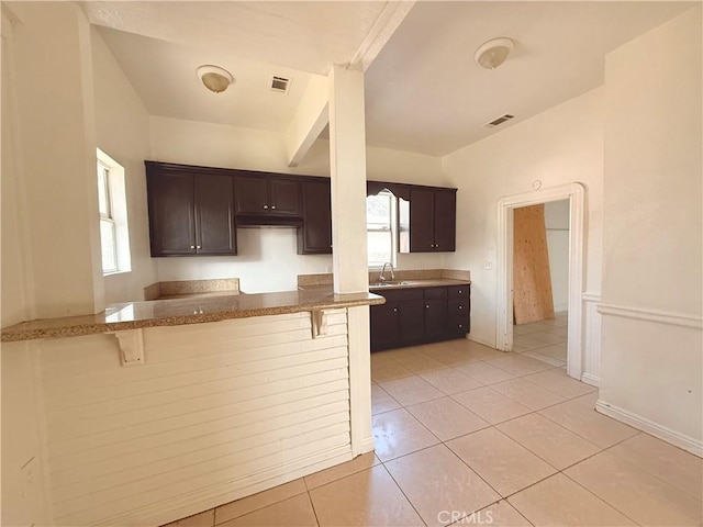 kitchen featuring light tile patterned flooring, dark brown cabinetry, a breakfast bar, sink, and kitchen peninsula