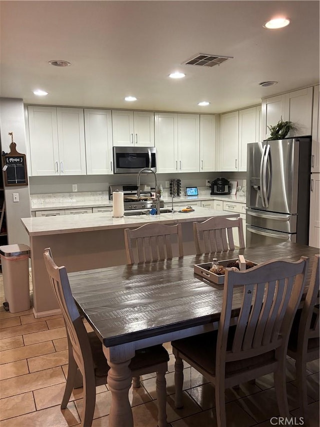 kitchen featuring white cabinetry, stainless steel appliances, and a kitchen island with sink