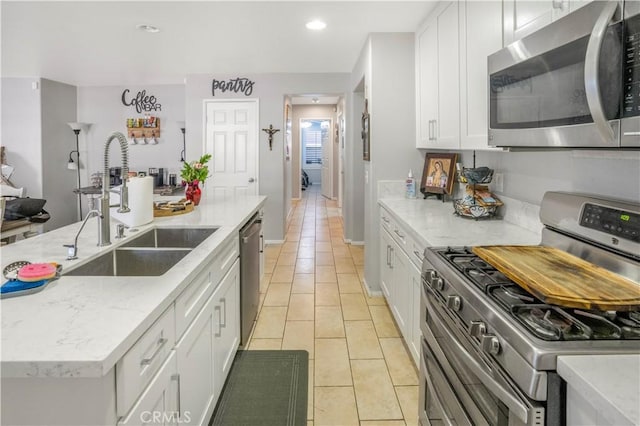 kitchen featuring light tile patterned floors, appliances with stainless steel finishes, white cabinets, and a sink