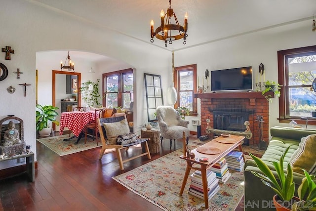 living room featuring plenty of natural light, dark wood-type flooring, a notable chandelier, and a fireplace