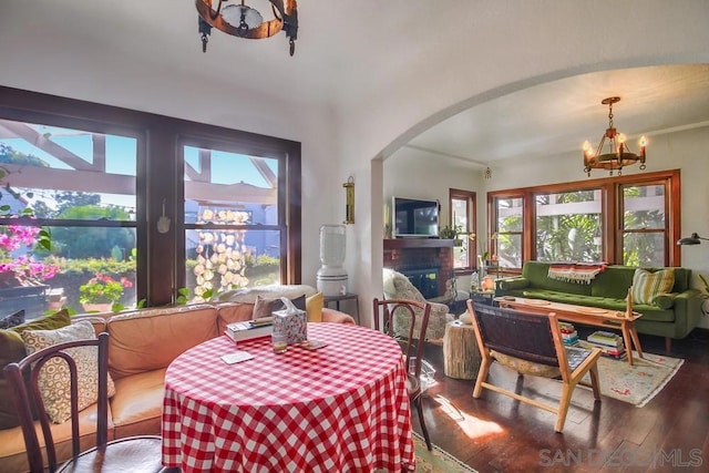 dining space with wood-type flooring, a healthy amount of sunlight, a notable chandelier, and a fireplace