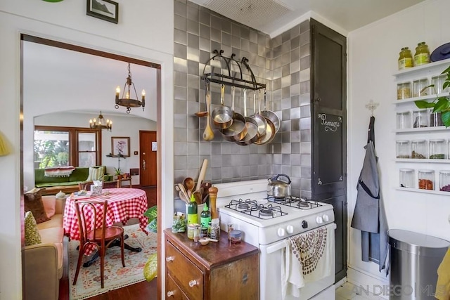 kitchen with wood-type flooring, tile walls, white gas range, a notable chandelier, and backsplash