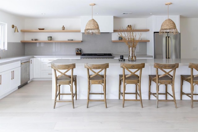 kitchen with pendant lighting, light hardwood / wood-style flooring, stainless steel appliances, a kitchen breakfast bar, and white cabinets