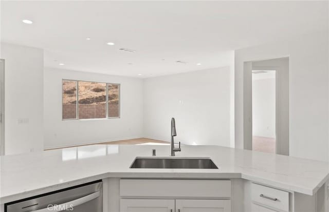 kitchen featuring light stone counters, dishwasher, sink, and white cabinets