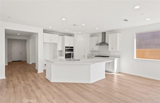 kitchen with white cabinets, black gas cooktop, a kitchen island with sink, and wall chimney range hood