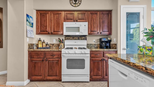 kitchen featuring white appliances, dark stone counters, and light tile patterned flooring