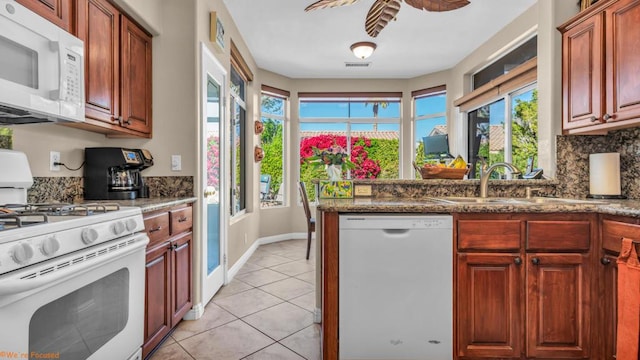 kitchen featuring sink, white appliances, light tile patterned floors, dark stone countertops, and tasteful backsplash