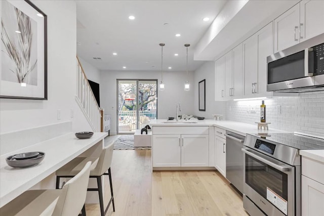 kitchen with pendant lighting, sink, appliances with stainless steel finishes, light hardwood / wood-style floors, and white cabinets