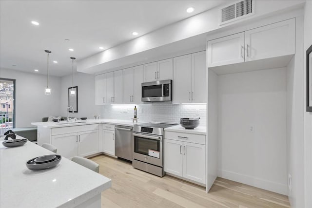 kitchen with sink, white cabinetry, stainless steel appliances, tasteful backsplash, and decorative light fixtures