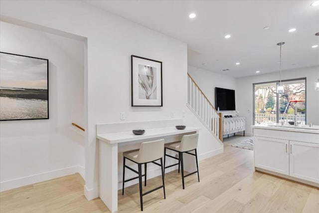 interior space with hanging light fixtures, a breakfast bar, white cabinets, and light wood-type flooring