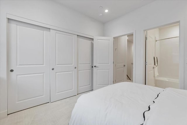 bedroom with ensuite bathroom, light colored carpet, and a closet