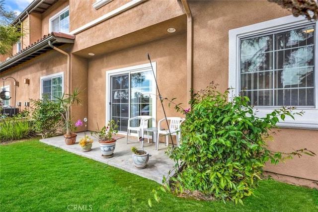 view of exterior entry featuring a lawn and a patio