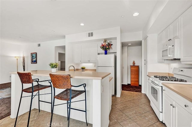 kitchen featuring sink, white appliances, light tile patterned floors, a breakfast bar, and white cabinetry