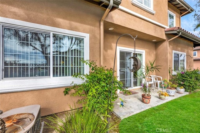 view of exterior entry featuring a patio area, central air condition unit, and a lawn