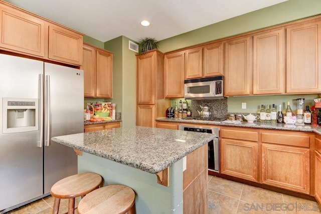 kitchen featuring a breakfast bar area, light stone counters, a kitchen island, stainless steel appliances, and backsplash