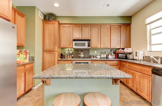 kitchen featuring a kitchen island, appliances with stainless steel finishes, sink, a kitchen breakfast bar, and light stone countertops