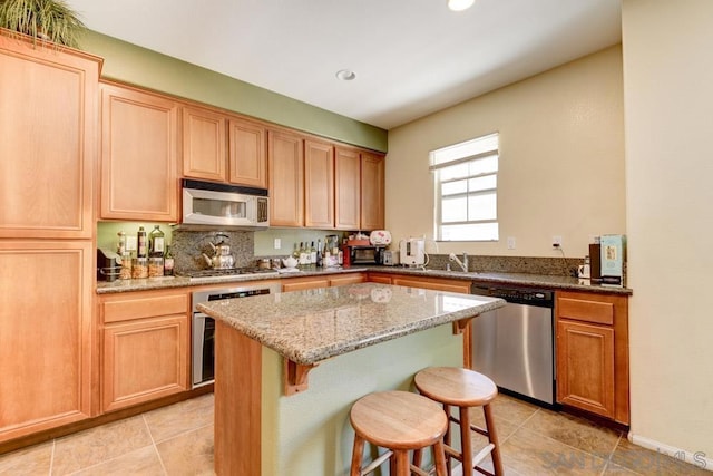 kitchen with light tile patterned floors, a kitchen island, stainless steel appliances, light stone countertops, and a kitchen bar