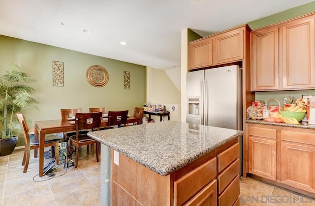 kitchen featuring light stone counters, light tile patterned floors, stainless steel fridge, and a center island