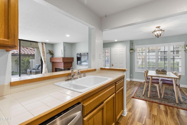 kitchen featuring sink, stainless steel dishwasher, tile counters, light hardwood / wood-style floors, and a brick fireplace