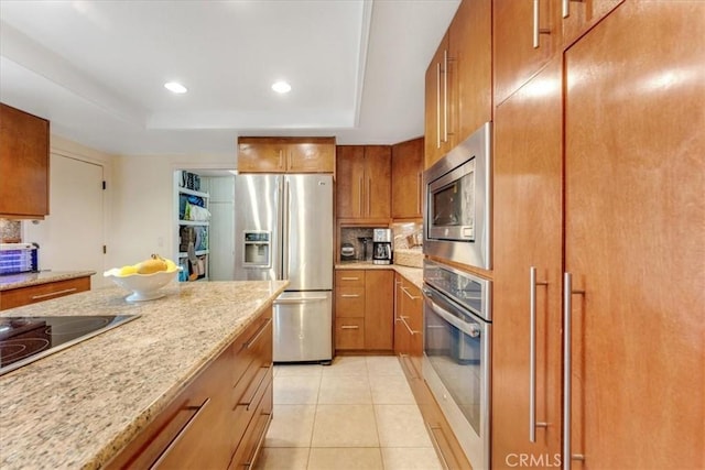 kitchen with light tile patterned floors, appliances with stainless steel finishes, tasteful backsplash, a tray ceiling, and light stone countertops