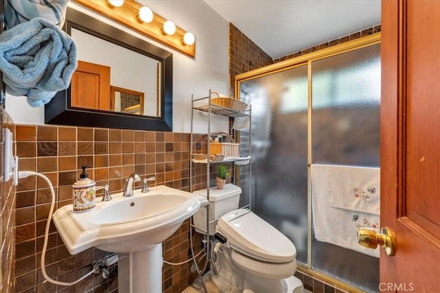 bathroom featuring toilet, sink, tile walls, and a shower with shower door