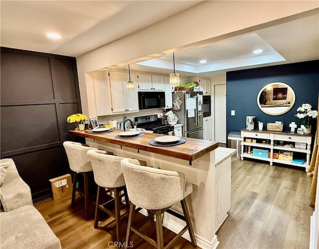 kitchen with white cabinetry, stainless steel appliances, decorative light fixtures, and a kitchen bar