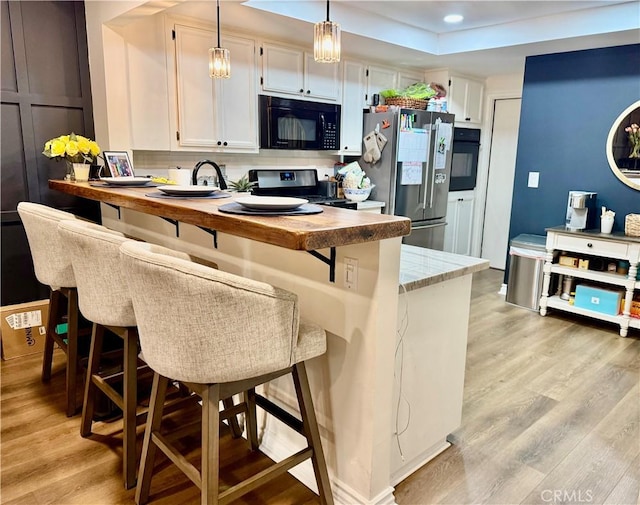 kitchen featuring decorative light fixtures, white cabinetry, decorative backsplash, black appliances, and light hardwood / wood-style flooring