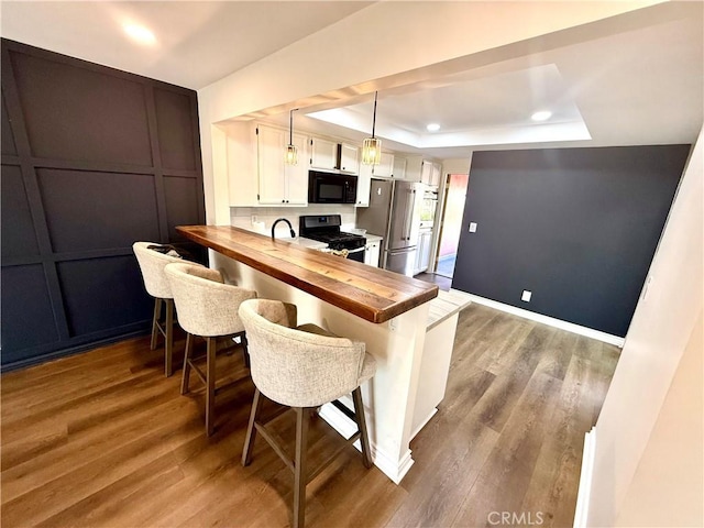 1430 E Foothill Blvd, Glendora, CA 91741 - kitchen featuring black appliances, a tray ceiling, wooden counters, wood finished floors, and a kitchen breakfast bar