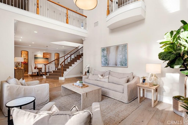 living room featuring a high ceiling, ornamental molding, and light hardwood / wood-style flooring