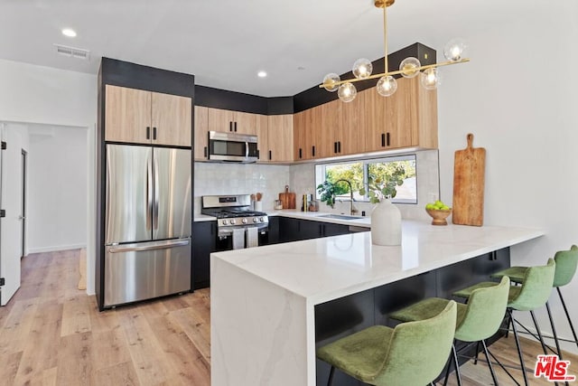 kitchen featuring a breakfast bar, sink, light hardwood / wood-style floors, kitchen peninsula, and stainless steel appliances