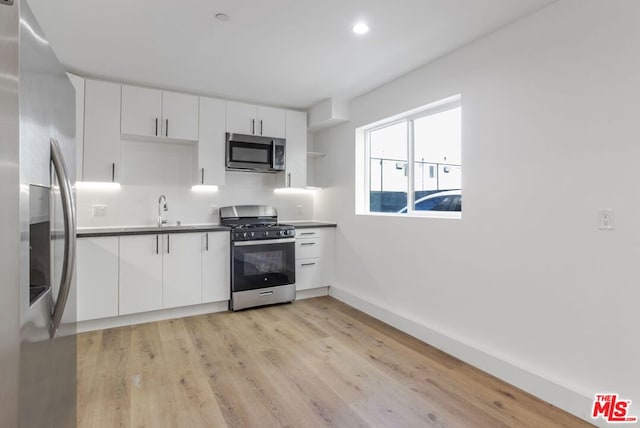 kitchen featuring white cabinetry, sink, stainless steel appliances, and light wood-type flooring