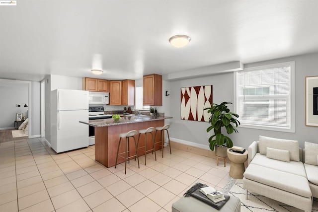 kitchen with light tile patterned floors, white appliances, a breakfast bar area, and kitchen peninsula