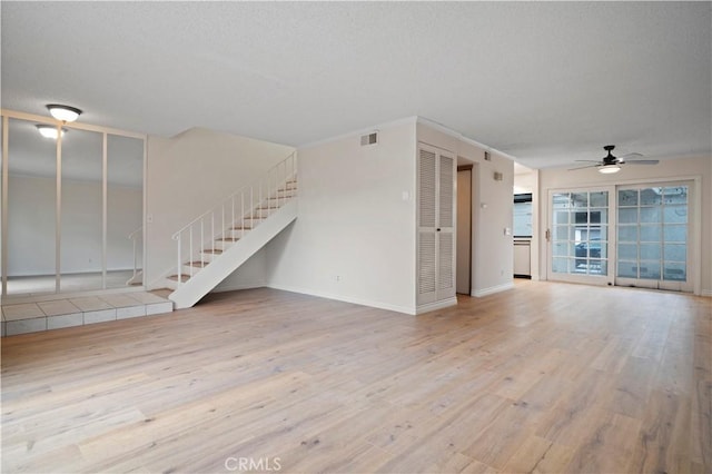 unfurnished living room with visible vents, a textured ceiling, wood finished floors, stairway, and ceiling fan