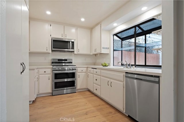 kitchen featuring light wood-type flooring, a sink, recessed lighting, appliances with stainless steel finishes, and light countertops