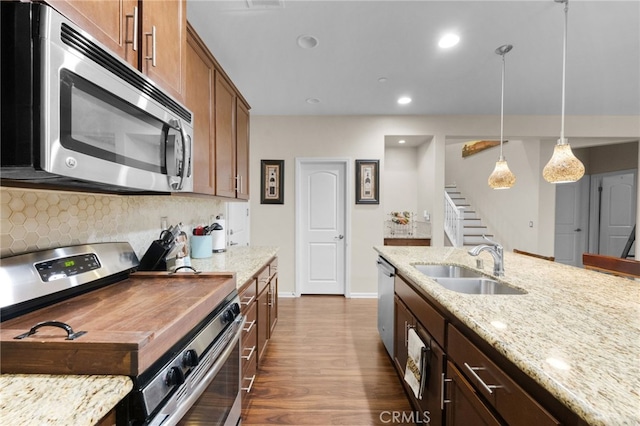 kitchen with sink, backsplash, hanging light fixtures, stainless steel appliances, and light stone countertops