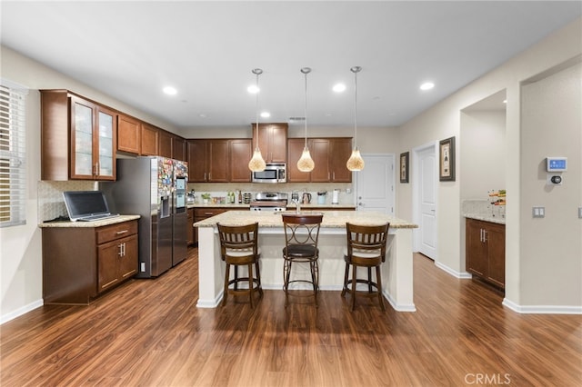 kitchen with a breakfast bar area, appliances with stainless steel finishes, a kitchen island with sink, light stone countertops, and decorative light fixtures