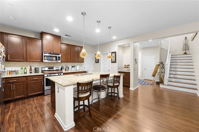 kitchen with appliances with stainless steel finishes, decorative light fixtures, a breakfast bar area, light stone countertops, and a center island with sink