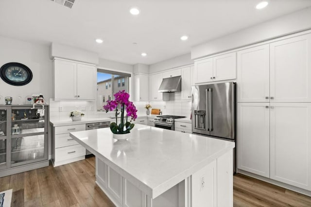 kitchen with high end appliances, white cabinetry, tasteful backsplash, a kitchen island, and light hardwood / wood-style floors