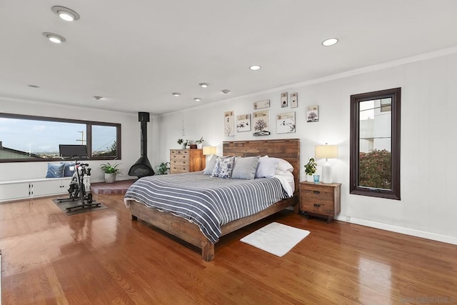 bedroom featuring hardwood / wood-style flooring, ornamental molding, and a wood stove