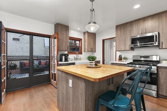 kitchen with appliances with stainless steel finishes, pendant lighting, wooden counters, and light wood-type flooring