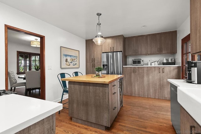 kitchen with butcher block counters, hanging light fixtures, a center island, stainless steel refrigerator with ice dispenser, and light hardwood / wood-style floors