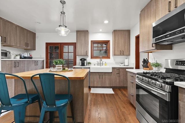 kitchen with a kitchen bar, sink, decorative light fixtures, light wood-type flooring, and appliances with stainless steel finishes