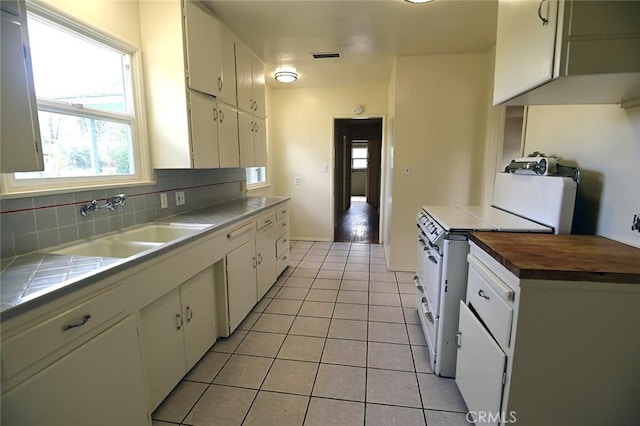 kitchen with sink, white cabinetry, light tile patterned floors, electric stove, and backsplash