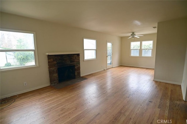 unfurnished living room featuring a stone fireplace, plenty of natural light, ceiling fan, and light wood-type flooring