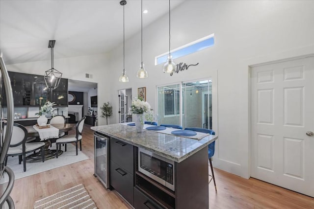 kitchen with pendant lighting, stainless steel appliances, a center island, light stone counters, and beverage cooler