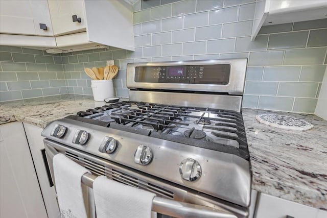 room details featuring white cabinets, light stone countertops, stainless steel gas range, and decorative backsplash