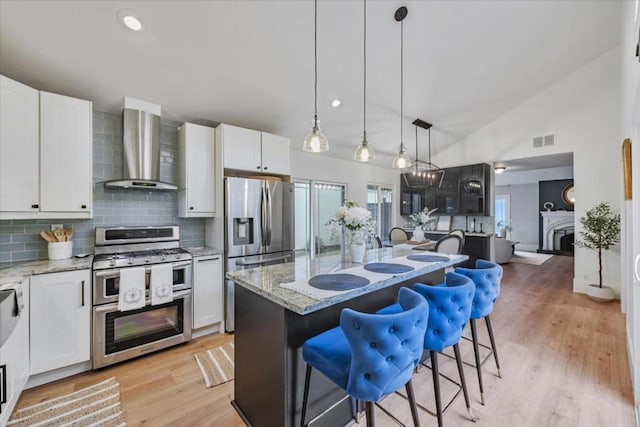 kitchen with a breakfast bar area, stainless steel appliances, wall chimney exhaust hood, and a center island with sink