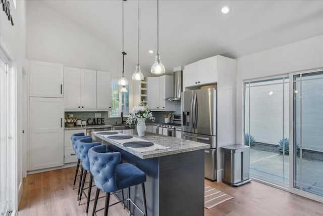 kitchen featuring white cabinetry, a center island, a kitchen breakfast bar, stainless steel appliances, and wall chimney range hood