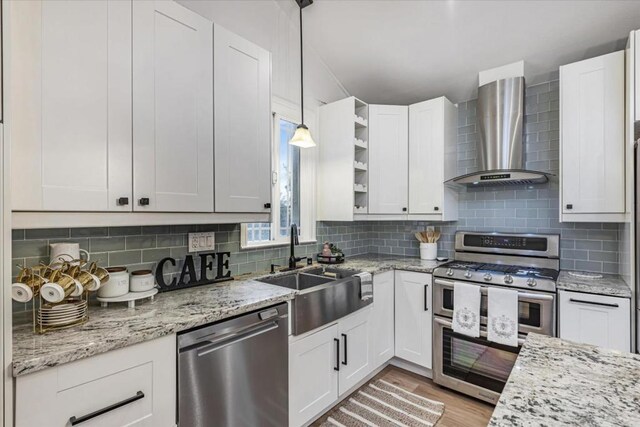 kitchen featuring stainless steel appliances, hanging light fixtures, wall chimney range hood, and white cabinets