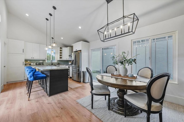 dining space with high vaulted ceiling, sink, and light hardwood / wood-style floors